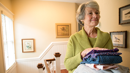 a smiling senior woman with a stack of folded clothes in her hands