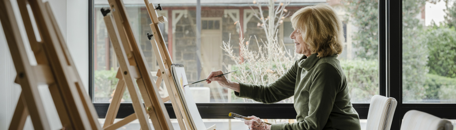 senior woman painting in an art room near a window