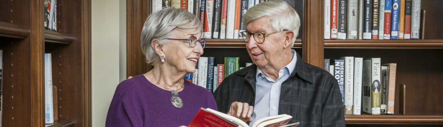 senior couple standing in front of bookshelves while reading together
