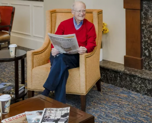 senior man reading the newspaper and smiling at someone off camera to his left