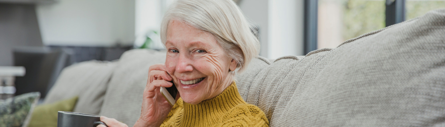 senior woman sitting on a couch and smiling at the camera while talking on a cell phone