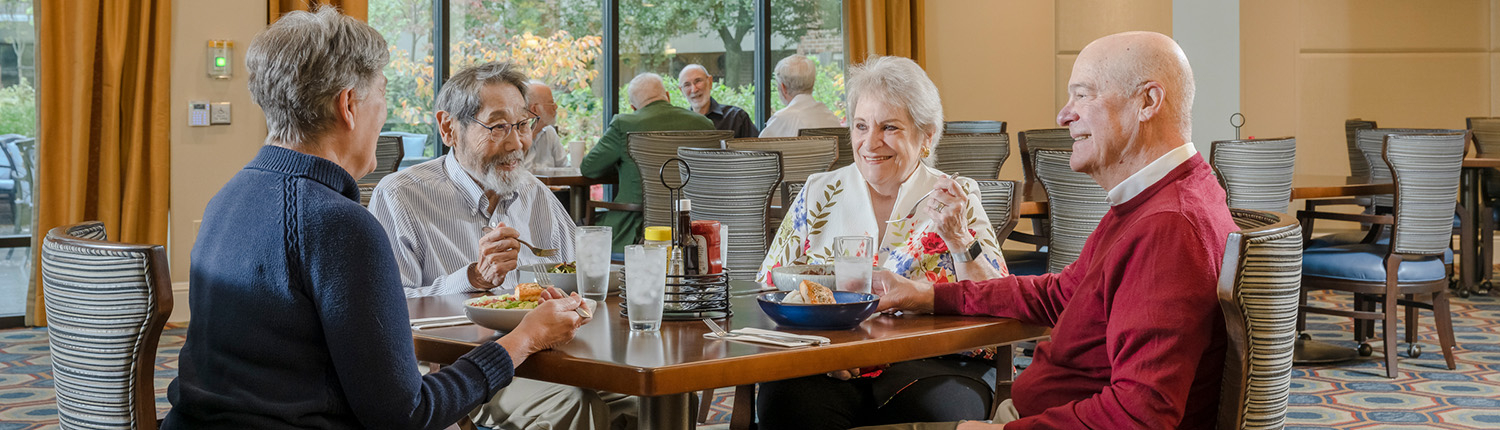 Image of a happy senior woman smiling and sitting at table visiting with a friend. 