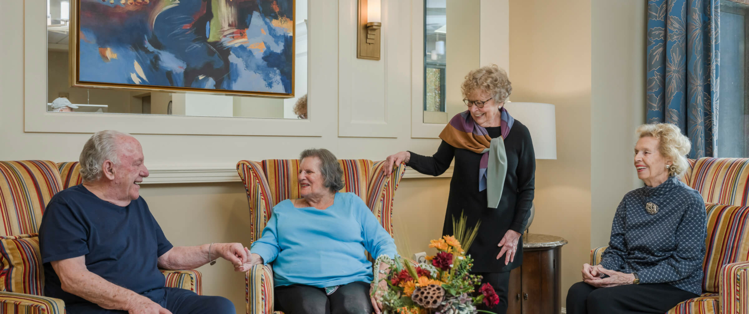 Photo of four senior friends visiting and laughing together in a common area at Roland Park Place, a senior living community in Baltimore