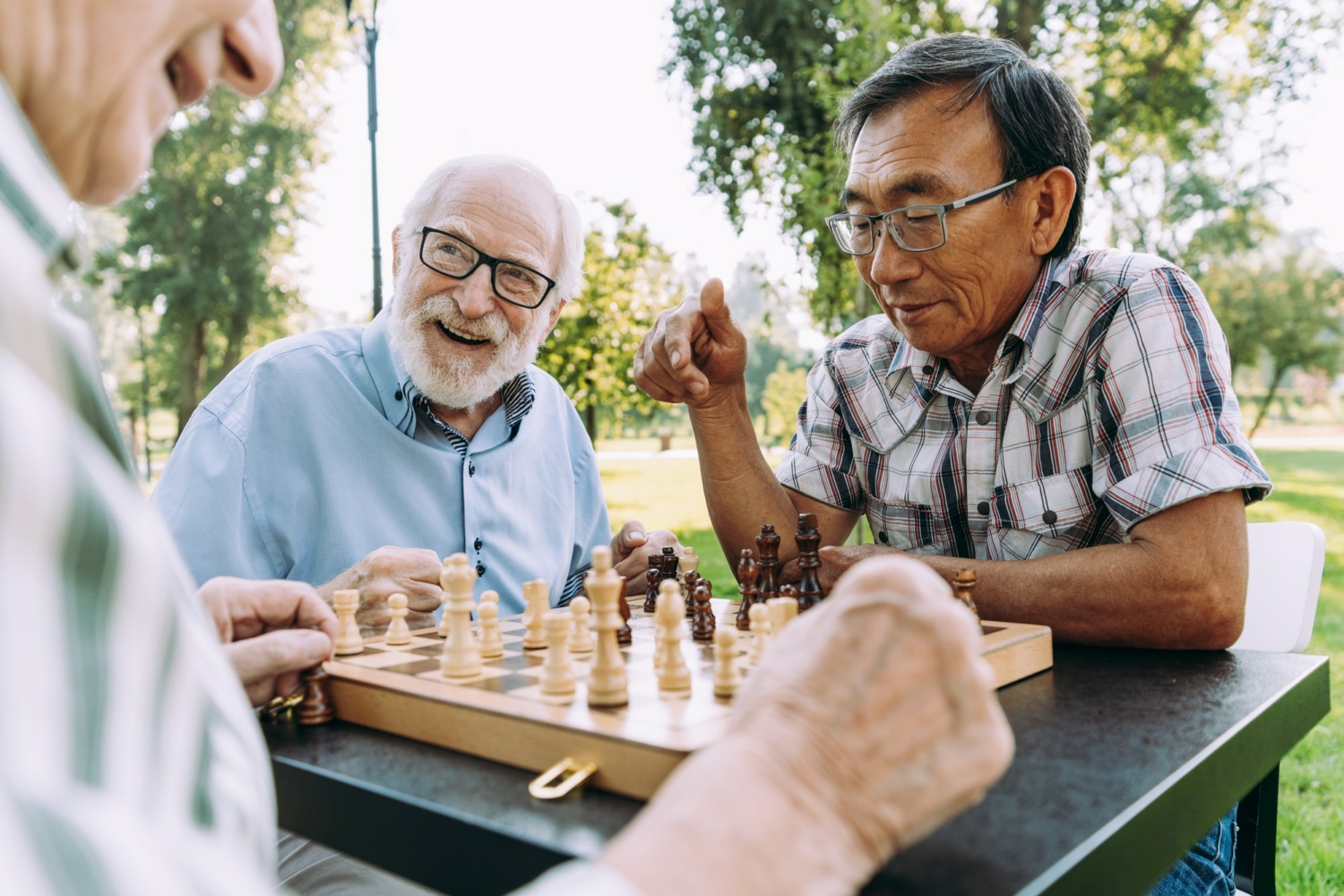 3 happy senior men sitting around a chess board at a table outdoors