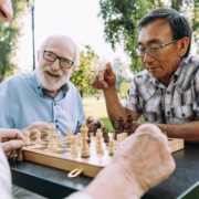 3 happy senior men sitting around a chess board at a table outdoors