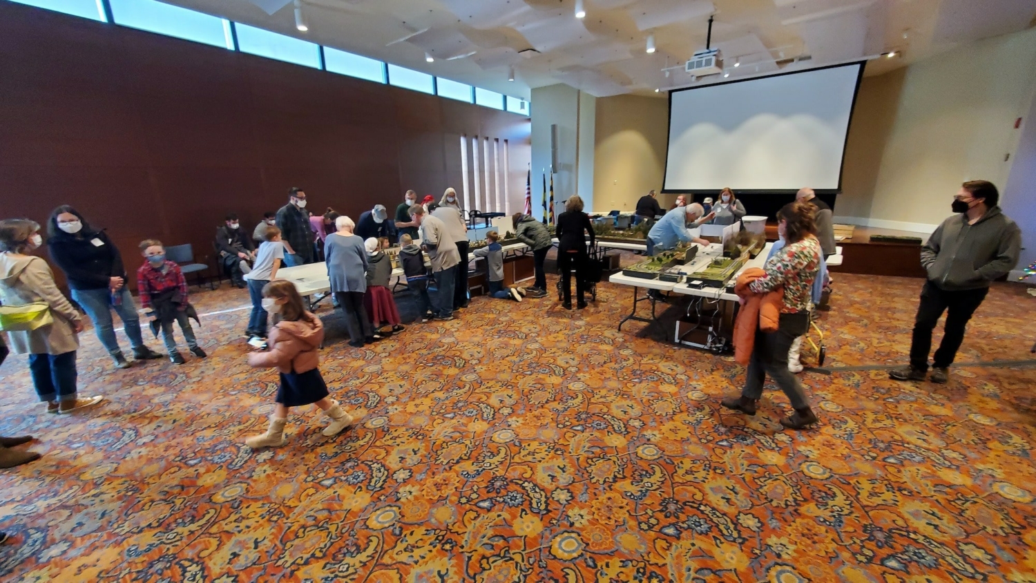 wide landscape photo showing all of the tables and people at our holiday model train show